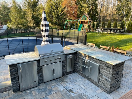 l shaped outdoor kitchen with combo storage and refrigerator next to pool on patio in stacked stone graphite